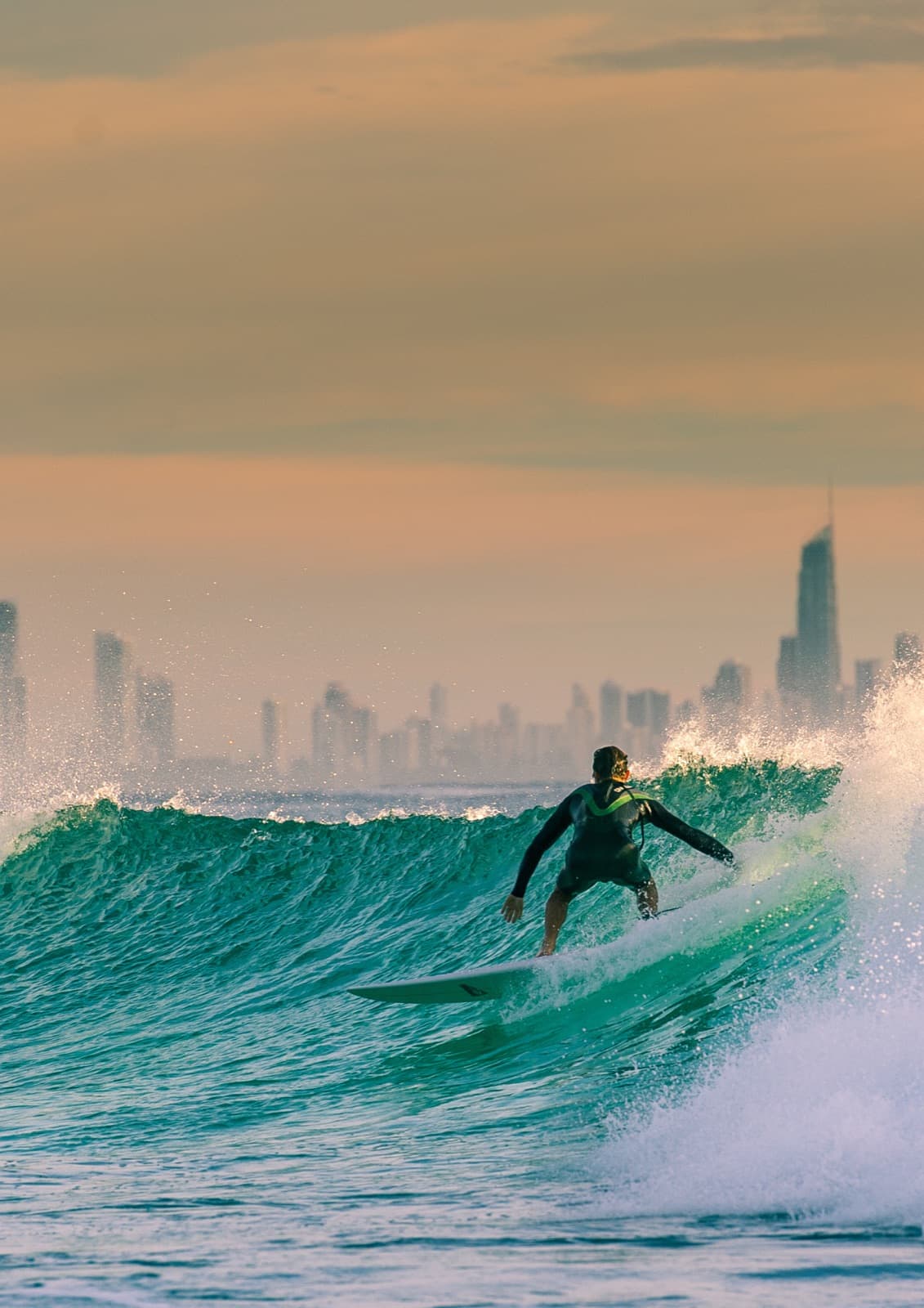 A surfer at sunrise with the Gold Coast skyline behind